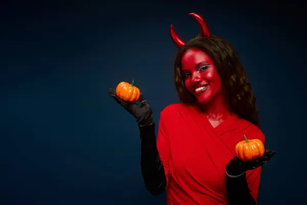 A beautiful woman, dressed as a devil, joyfully holds pumpkins, embracing the Halloween spirit. — Stock Photo