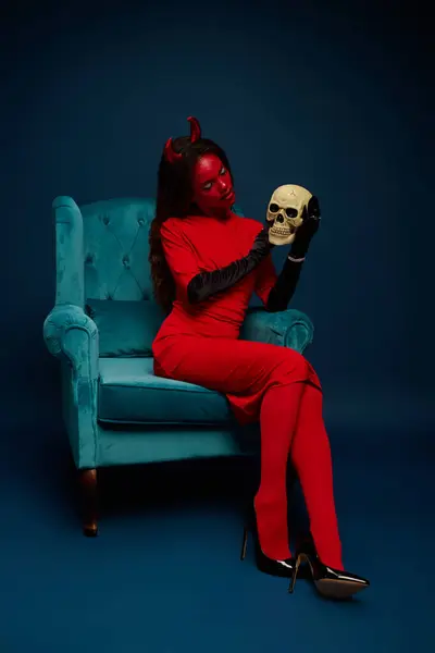 A stunning woman dressed in red with horns embraces a skull, radiating Halloween spirit. — Stock Photo