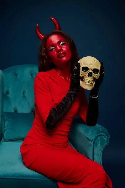 A beautiful woman dressed as a devil showcases her spooky costume while holding a skull. — Stock Photo