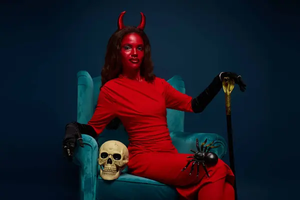 A devilish figure lounges gracefully amidst spooky decorations in a vibrant scene. — Stock Photo