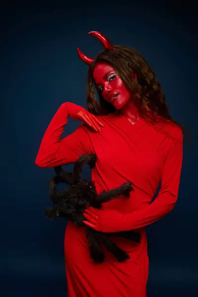 A captivating woman in red playfully shows a black spider, embodying Halloween spirit. — Stock Photo