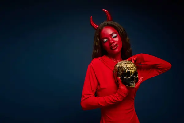 A mesmerizing woman showcases her Halloween look, featuring vivid red attire and a skull. — Stock Photo