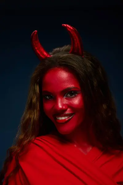 A woman in a striking red Halloween costume shows her playful spirit with devil horns. — Stock Photo