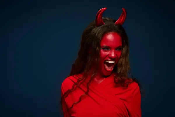 A stunning woman showcases her Halloween spirit with a bold devil costume, exuding energy and joy. — Stock Photo