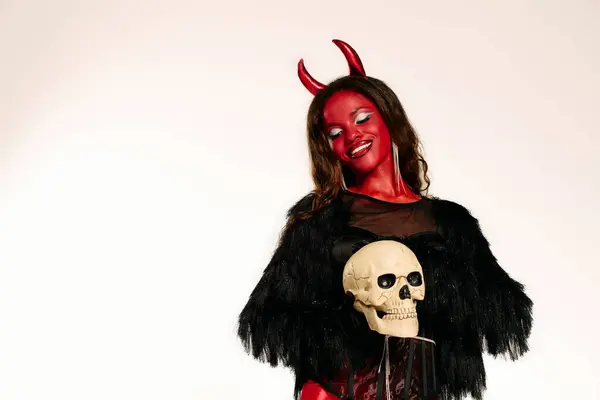 A beautiful woman embodies a devilish character, executing a captivating pose with a skull. — Stock Photo