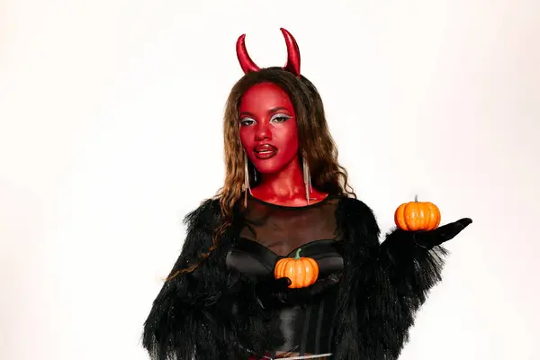A stunning woman in a devil costume showcases her creativity with pumpkins this Halloween. — Stock Photo
