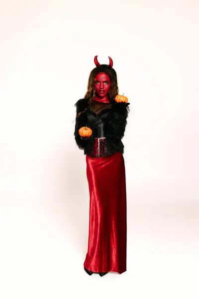 A stunning woman dressed in a devil costume holds two pumpkins, capturing the Halloween spirit. — Stock Photo