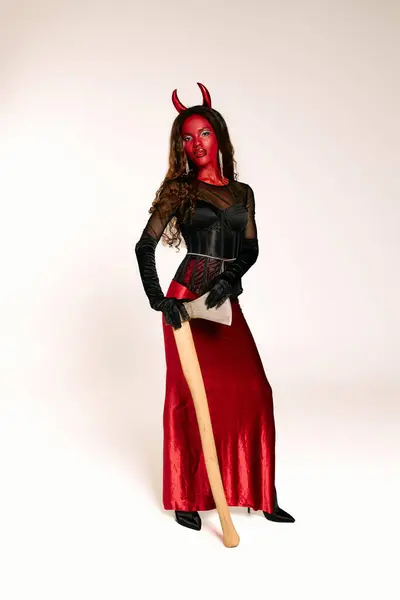 Uma mulher deslumbrante em um traje do diabo empunha um morcego com confiança em um evento de Halloween. — Fotografia de Stock