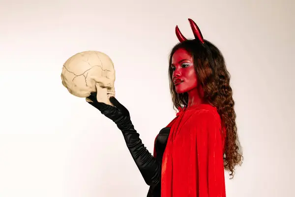Dressed in a striking devil costume, a woman showcases her Halloween spirit by holding a skull. — Stock Photo