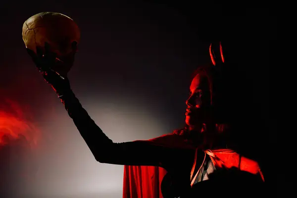 A striking woman showcases her Halloween costume, holding a skull under moody, atmospheric lighting. — Stock Photo