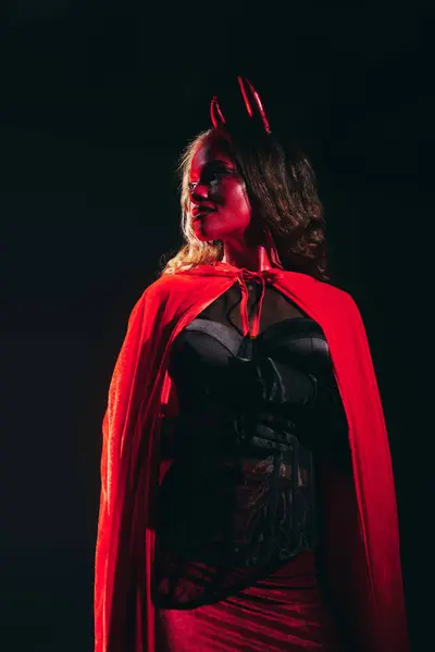 A stunning woman, dressed as a devil, strikes a powerful pose against a dark background. — стоковое фото