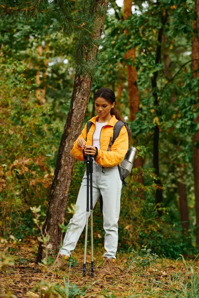 In mezzo al fogliame colorato, una giovane donna si ferma con bastoni da trekking, abbracciando la bellezza della natura in autunno.. — Foto stock