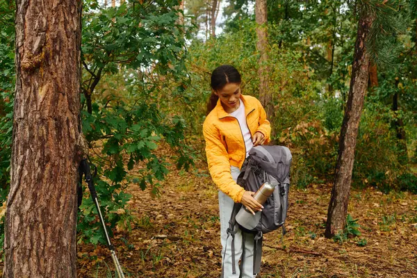 A young woman explores a vibrant autumn forest, preparing her backpack for an exciting hiking adventure. — Stock Photo
