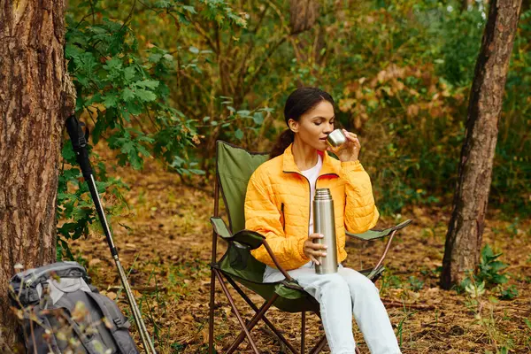 Una giovane donna sorseggia da una tazza mentre si rilassa in una foresta piena di fogliame autunnale. — Foto stock