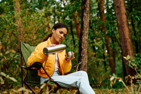 Rodeada de coloridas hojas otoñales, una mujer se relaja con una bebida caliente mientras camina por el bosque. - foto de stock