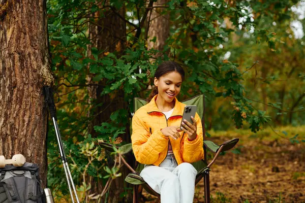 Rodeada por cores vibrantes de outono, uma jovem relaxa enquanto verifica seu telefone na floresta. — Fotografia de Stock