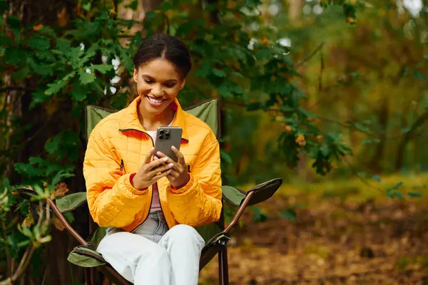 Une jeune femme joyeuse repose sur une chaise de camping tout en explorant la beauté de la nature en automne. — Photo de stock