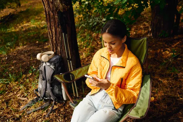 Uma jovem relaxa na floresta, deliciando-se com a natureza enquanto verifica seu telefone em meio a tons de outono. — Fotografia de Stock