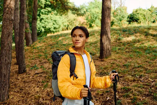 Una giovane donna si gode un'escursione in una colorata foresta autunnale, circondata da foglie d'oro e alberi alti. — Foto stock