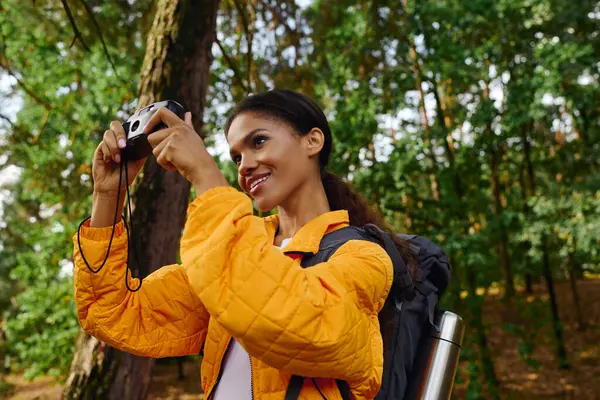 Una giovane donna afroamericana ama fare escursioni attraverso una foresta colorata, catturando lo splendido paesaggio autunnale.. — Foto stock