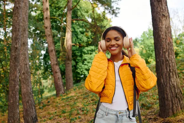 A joyful young woman listens to music while hiking through a vibrant autumn forest bursting with color. — Stock Photo