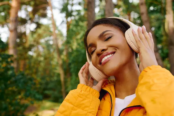 Una giovane donna sorride gioiosa in una foresta vibrante, abbracciando l'aria autunnale ascoltando musica. — Foto stock