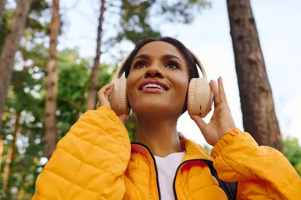 Une jeune femme joyeuse avec un sourire lumineux embrasse la nature et la musique tout en faisant de la randonnée dans une forêt d'automne colorée. — Photo de stock