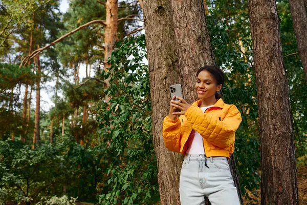 A young African American woman enjoys her time hiking, surrounded by autumn colors in a forest. — Stock Photo