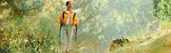 An adventurous young woman hikes through a colorful autumn forest filled with trees and sunlight. — Stock Photo