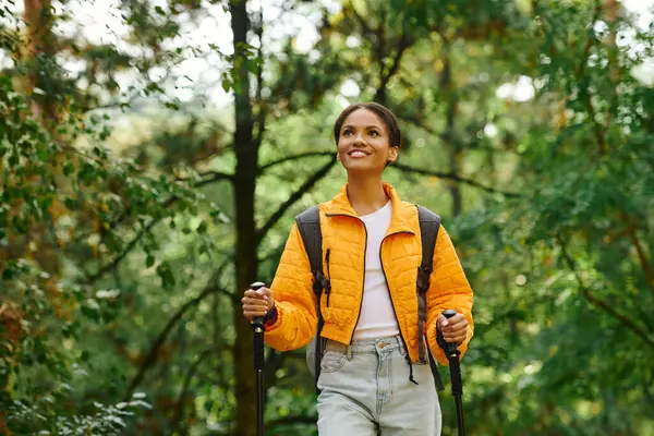 Una giovane donna abbraccia la bellezza dell'autunno mentre cammina attraverso una foresta lussureggiante, irradiando gioia e avventura. — Foto stock