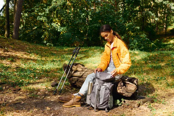A determined young woman explores a vibrant forest, adjusting her gear amidst the autumn foliage. — Stock Photo
