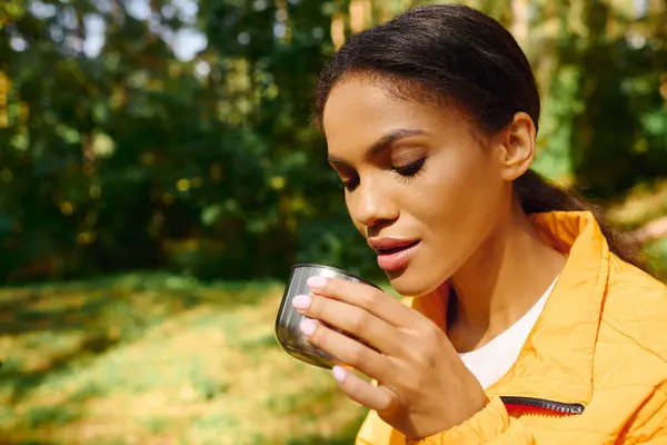 In a colorful autumn forest, a young woman savors a warm drink during her hiking adventure. — Stock Photo