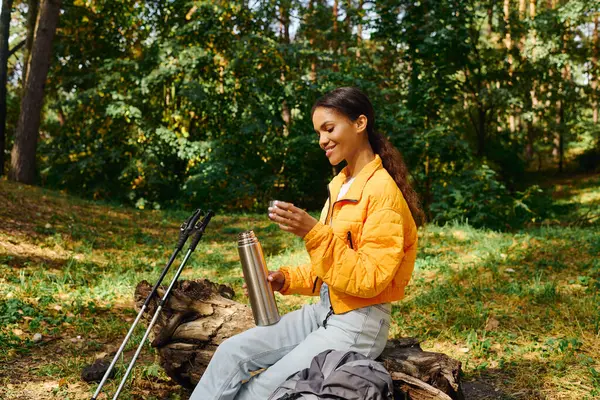 Si siede su un tronco caduto nella foresta, assaporando una bevanda calda circondata da foglie autunnali colorate. — Foto stock