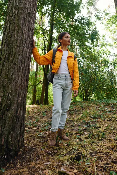 A young African American woman stands confidently in an autumn forest, enjoying her hiking adventure. — Stock Photo