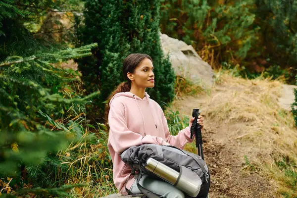 A young African American woman pauses while hiking through a colorful autumn forest, taking in the surroundings. — Stock Photo