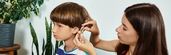A mother lovingly assists her young son with his hearing aid in a nurturing environment. — Stock Photo