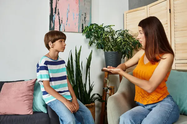 Eine Mutter bringt ihrem schwerhörigen Sohn im gemütlichen Wohnzimmer Zeichensprache bei. — Stockfoto