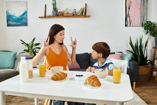 A mother engages with her hearing impaired son using sign language while sharing breakfast. — Stock Photo