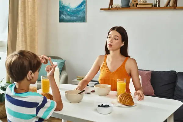 Un niño usa el lenguaje de señas para comunicarse con su atenta madre durante el desayuno.. - foto de stock
