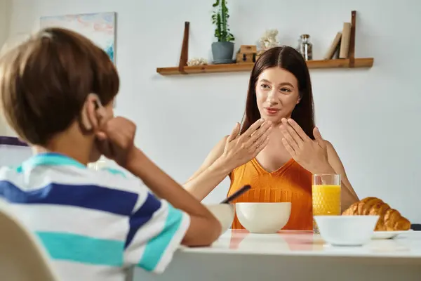 Um menino se envolve com sua mãe enquanto ela usa linguagem gestual enquanto eles compartilham uma refeição do café da manhã. — Fotografia de Stock