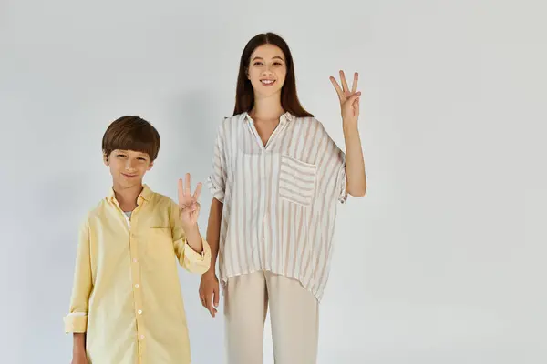 A little boy with hearing impairment poses beside his mother, both beaming and making peace signs. — Stock Photo