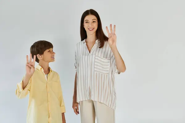 Um garotinho orgulhosamente exibe um sinal de paz ao lado de sua mãe carinhosa, ambos sorrindo calorosamente. — Fotografia de Stock