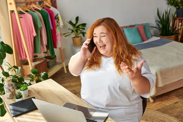 A plus size woman is joyfully chatting on her phone in a warm, inviting space full of greenery. — Stock Photo