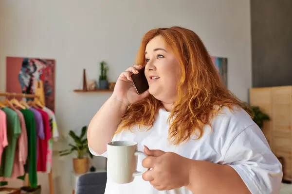 A beautiful plus size woman talks on the phone, savoring her coffee in a charming space. — Stock Photo