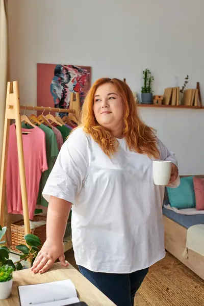 The beautiful plus size woman relaxes with a cup in a stylish indoor setting, exuding confidence. — Stock Photo