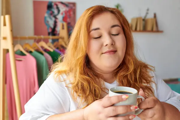 A plus size woman with flowing hair enjoys a warm cup of coffee, radiating happiness and comfort. — Stock Photo
