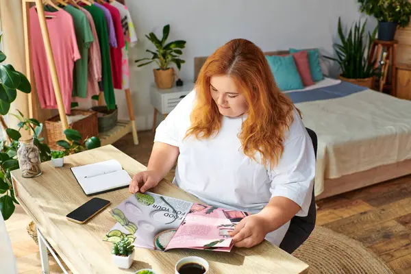 В уютной комнате женщина plus size ценит красочный журнал, потягивая кофе. — стоковое фото