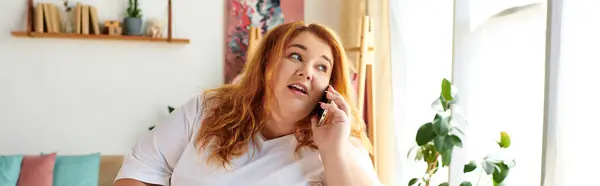 A beautiful plus size woman talks animatedly on the phone, bright sunlight streaming in. — Stock Photo