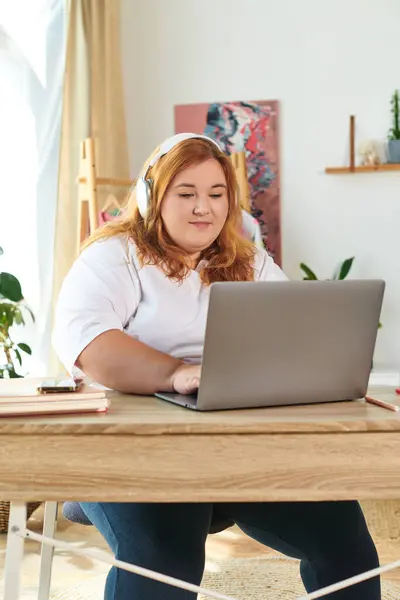 Una mujer segura de tamaño grande en un escritorio, enfocada en su computadora portátil con auriculares. — Stock Photo