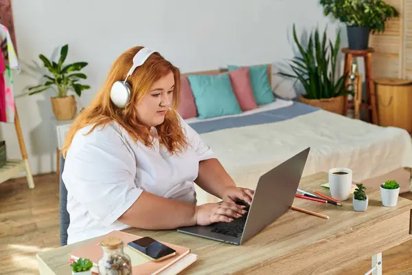 Прекрасная женщина plus size фокусируется на своем ноутбуке в современном, приглашающем домашнем офисе, заполненном растениями. — стоковое фото
